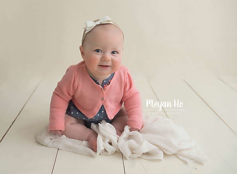 smiling sitting baby girl in pink cardigan on white wood in southern nh