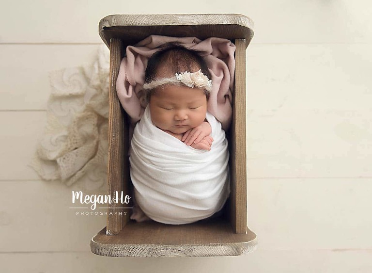 sweet wrapped sleeping baby girl in white in little wood bed with pink blanket