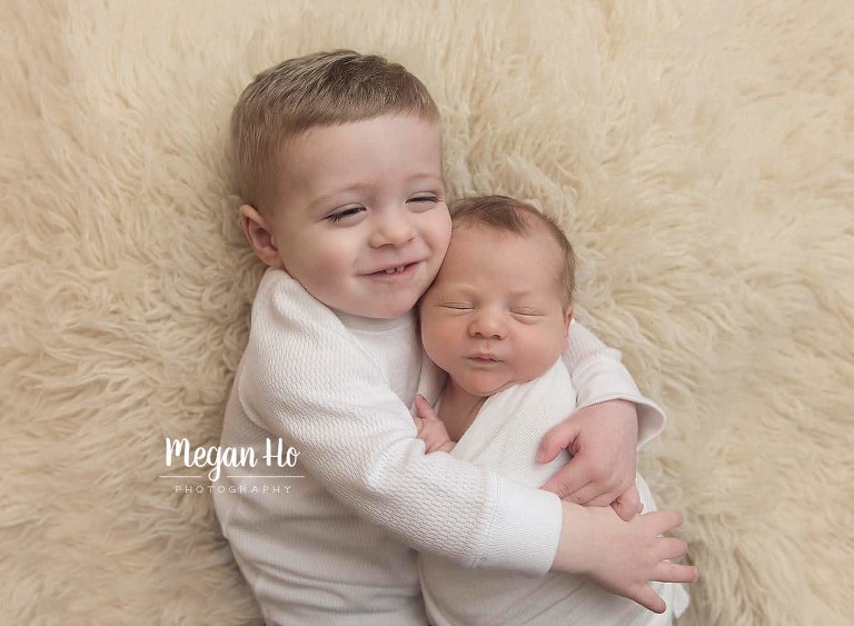 sweet brothers snuggling in white laying on white fluffy rug in newborn session