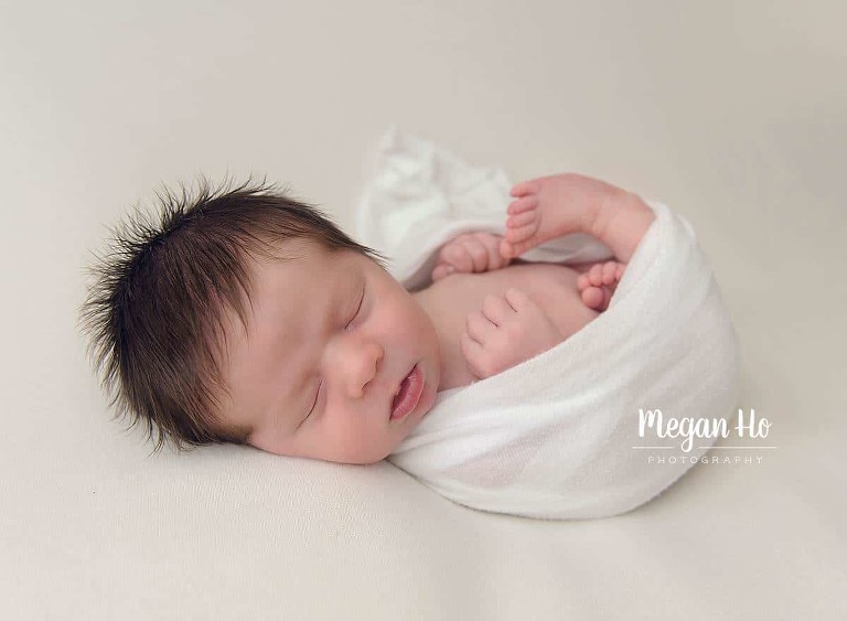 sweet sleeping baby boy wrapped in white with adorable brown hair