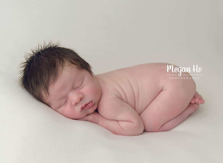 sleepy naked baby boy in bum up pose with lots of brown hair