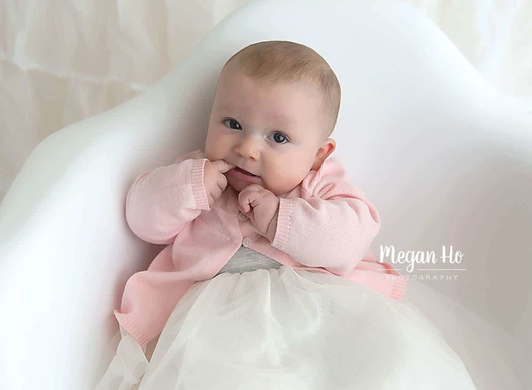 baby girl sitting up in chair with finger in her mouth in southern nh