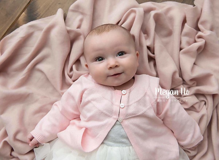 sweet six month girl in pink cardigan laying on pink fabric on the floor