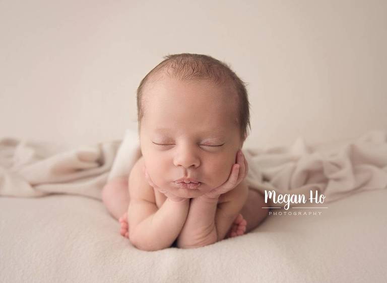 beautiful newborn boy in froggy pose with head in hands on tan