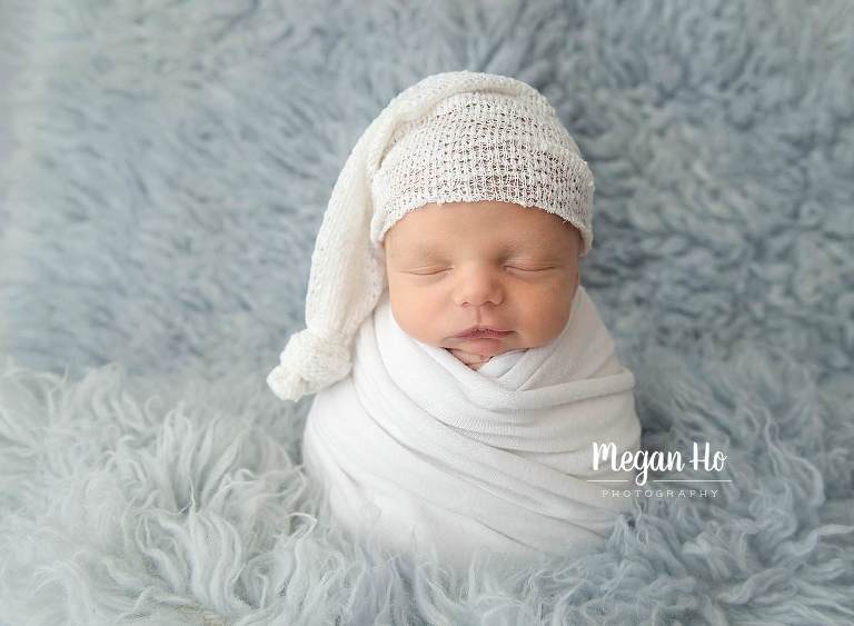 adorable baby boy wrapped up in white with sleepy cap on blue flokati