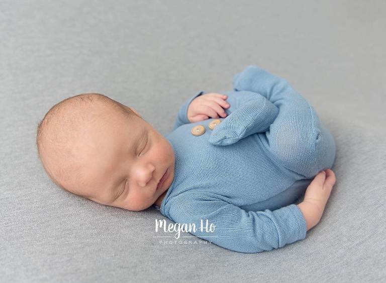 baby blue romper on newborn boy sleeping on back with legs tucked up