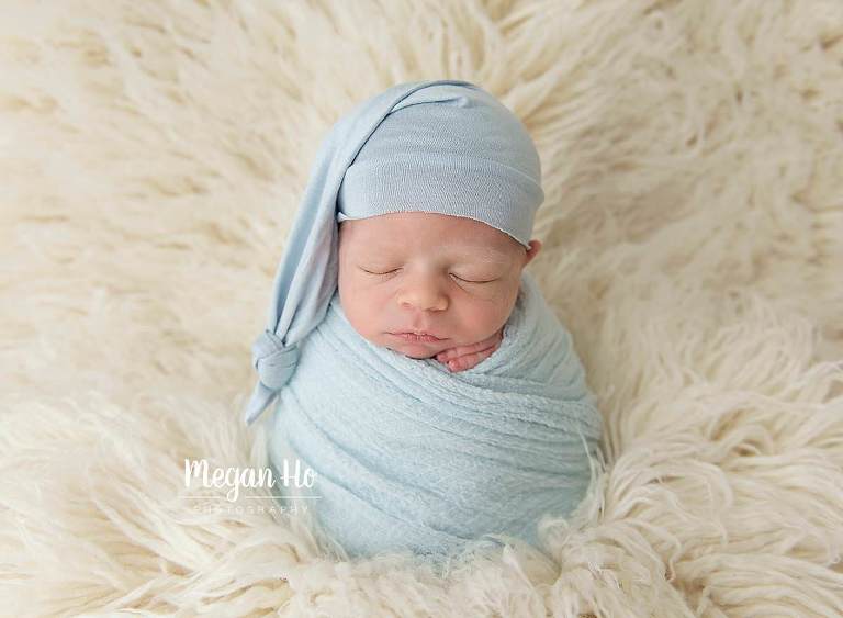 baby boy in potato sack in light blue wrap and hat on rug in bedford nh