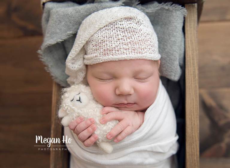 little newborn boy holding white sheet stuffy while sleeping with little hat on