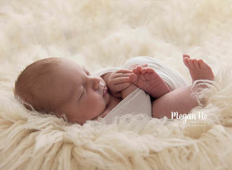 backlit shot of newborn boy with feet out snuggled in white flokati rug