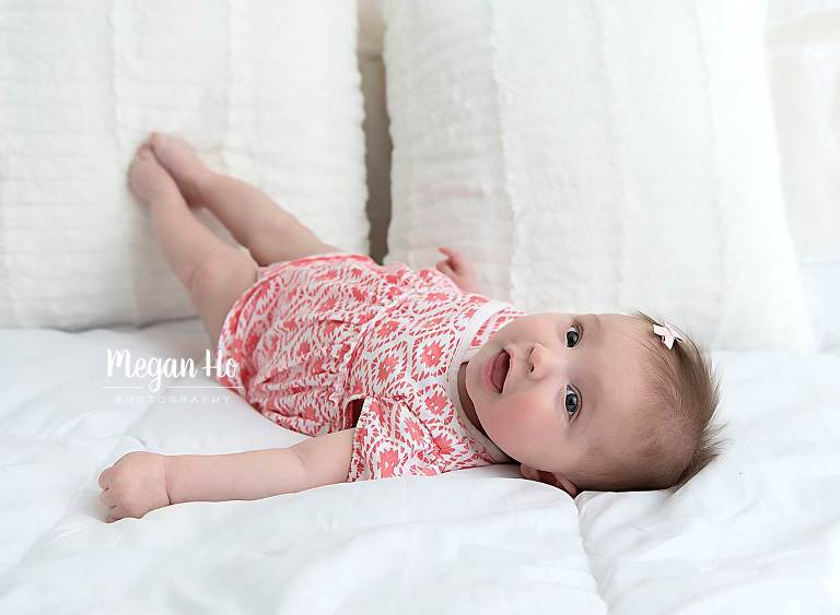 baby girl smiling and laying on back with toes touching white pillows