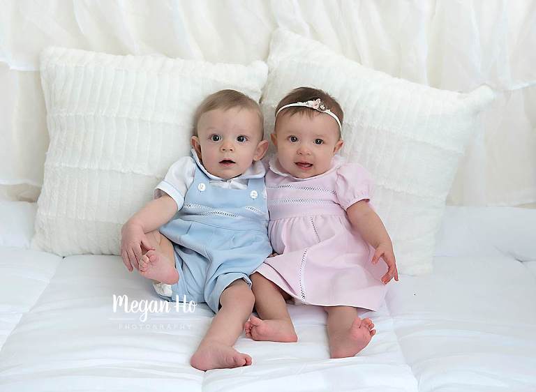 boy and girl twins in adorable pink and blue outfits on white bed in nh studio
