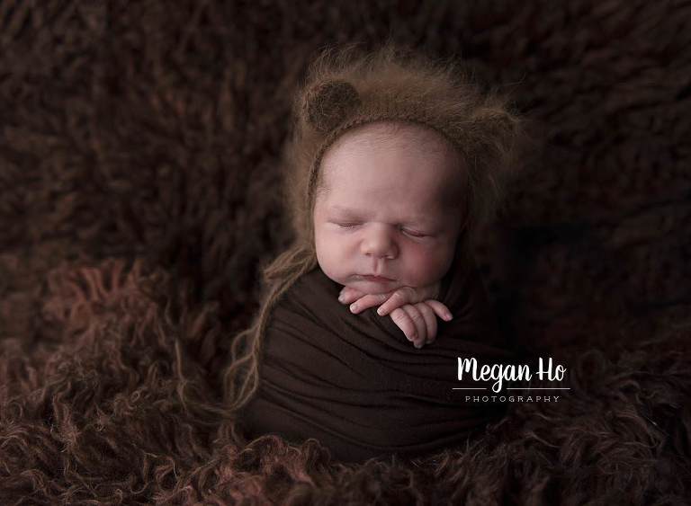 baby boy wrapped in brown with knit bear hat on sleeping on brown rug
