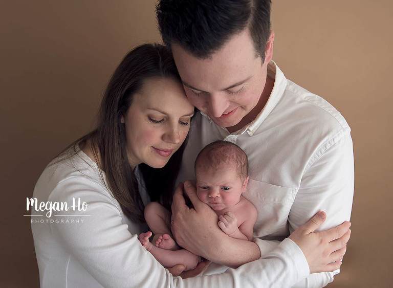 mom and dad staring lovingly at baby boy on brown background