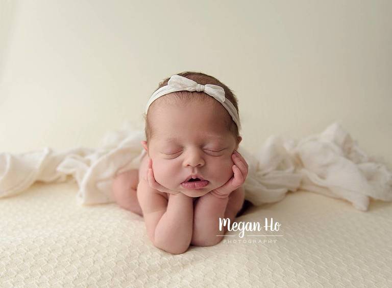 baby girl in froggy pose with white bow on soft blanket