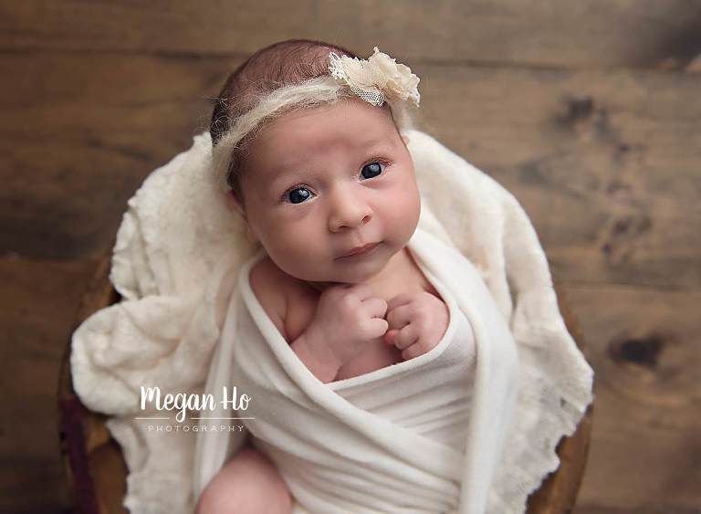 beautiful baby girl in wooden bowl in neutral setup with eyes wide open