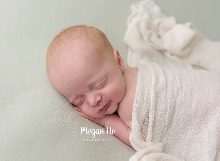 little boy sleeping with light blanket over back with adorable little smile