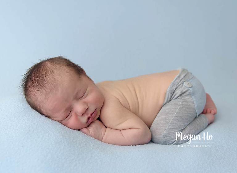 baby boy curled up on belly with little grey and blue pants on in newborn session