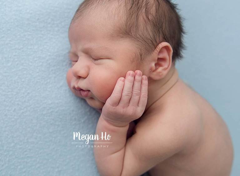 tiny little fingers resting on big baby cheeks with close up of sleeping newborn boy