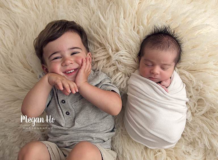 brothers laying on fluffy white rug together in bedford nh newborn session