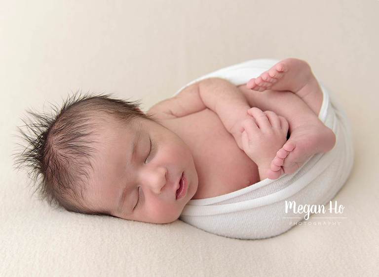 sleeping little boy wrapped in white with arms and legs out on brown blanket