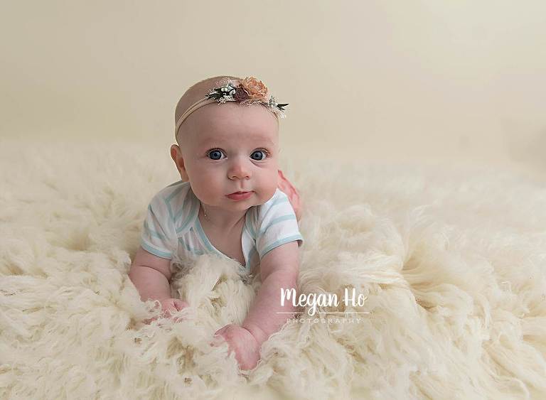 cute little girl pushing up at four months in peach and green on white rug
