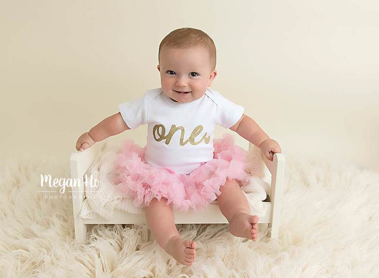 adorable little girl in pink tutu sitting on little white bed on fluffy rug