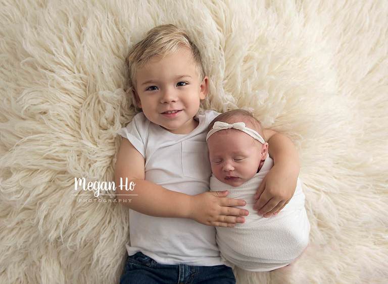 little boy in white snuggling newborn baby sister in newborn studio