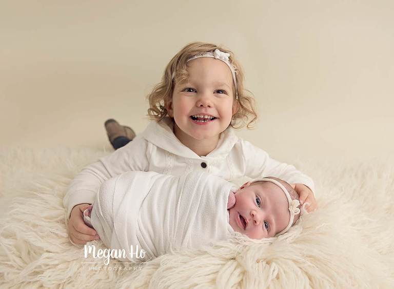 happy smiling siblings in nh newborn session laying on white fluffy rug
