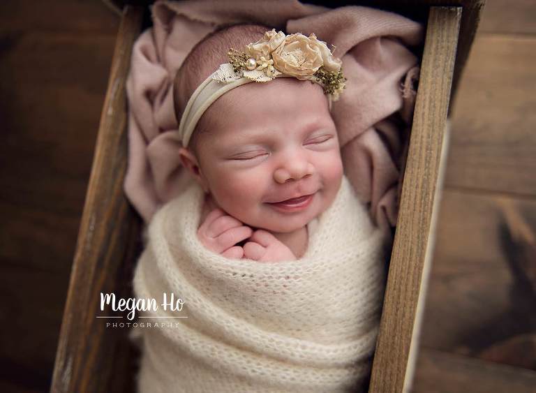 newborn in nh session wrapped in white knit wrap in wooden bed