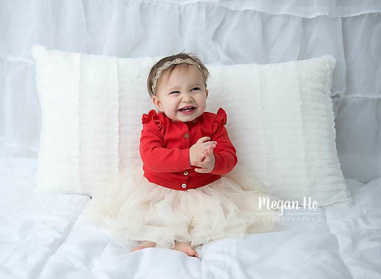 happy one year girl in red and white sitting on white bed
