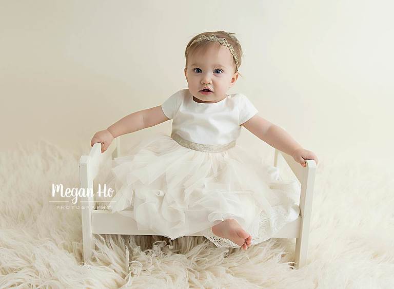smiling girl sitting on bed in white one year session