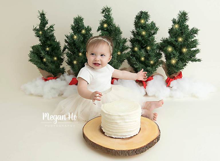Christmas cake smash baby girl with cake in front of Christmas trees