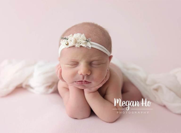 newborn girl sleeping in froggy pose on light pink background