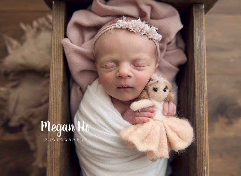 sweet baby girl in light pink snuggling with little doll in bed on wood floor