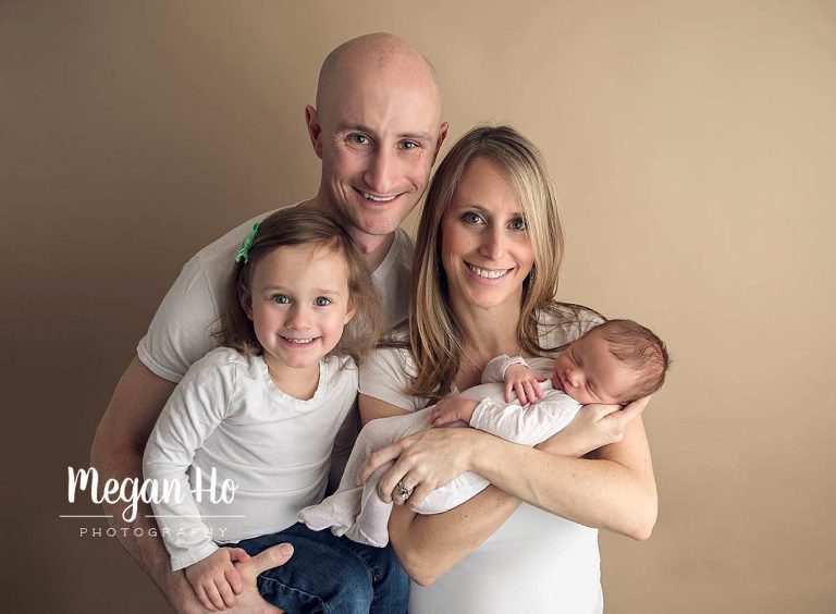 adorable family of four all in white smiling with brand new baby
