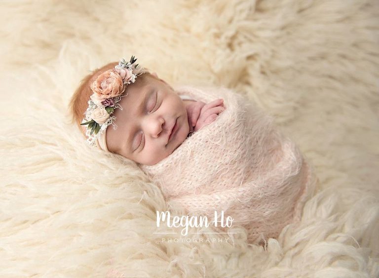 grinning little girl wrapped in knit wrap sleeping on shaggy rug