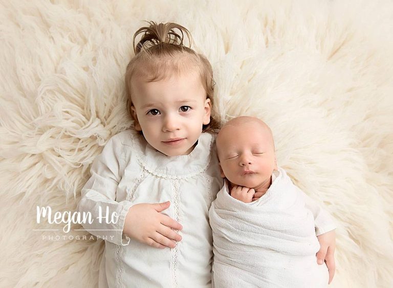 big sister snuggling her baby brother in newborn session on white
