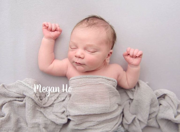 sleeping baby boy on back with arms up with draped fabric