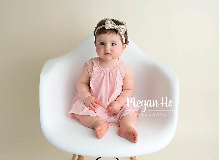 baby girl sitting up in pink dress sitting on little white chair