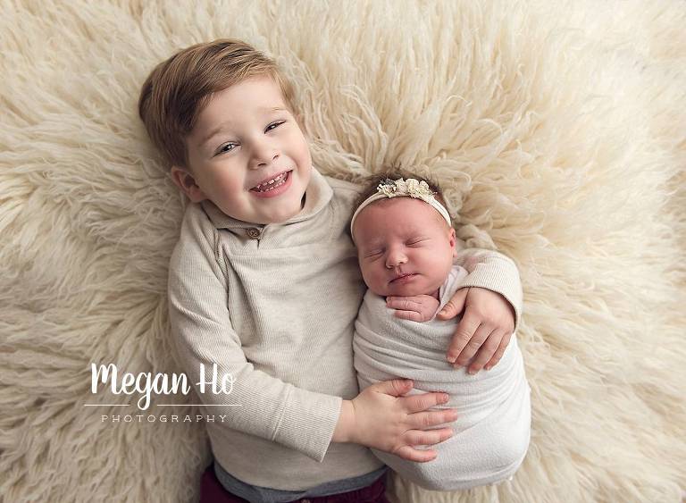 sweet big brother holding newborn sister all in neutrals