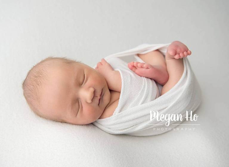 adorable sleeping baby boy wrapped in white with little toes showing